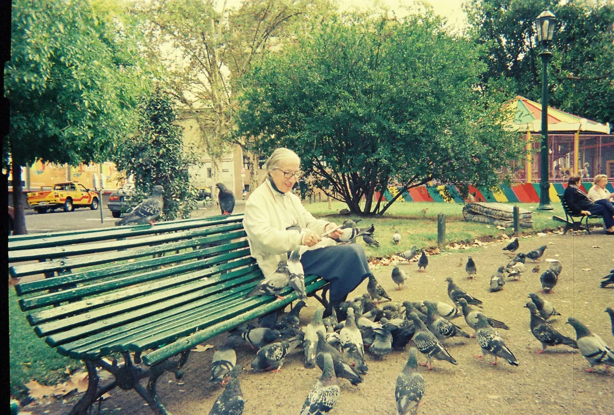 Una persona en un banco rodeada de palomas en la Plaza Barrientos, Recoleta